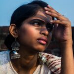 Striking portrait of a woman wearing large earrings and ethnic attire in sunlight.