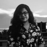 Monochrome portrait of a woman outdoors wearing a floral shirt, captured in dramatic lighting.